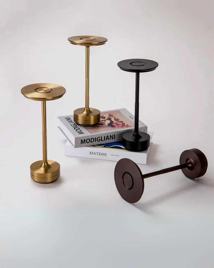 LumiHikari Base Lamp collection in brushed metal finishes with minimalist design, arranged on a white surface and atop art books.