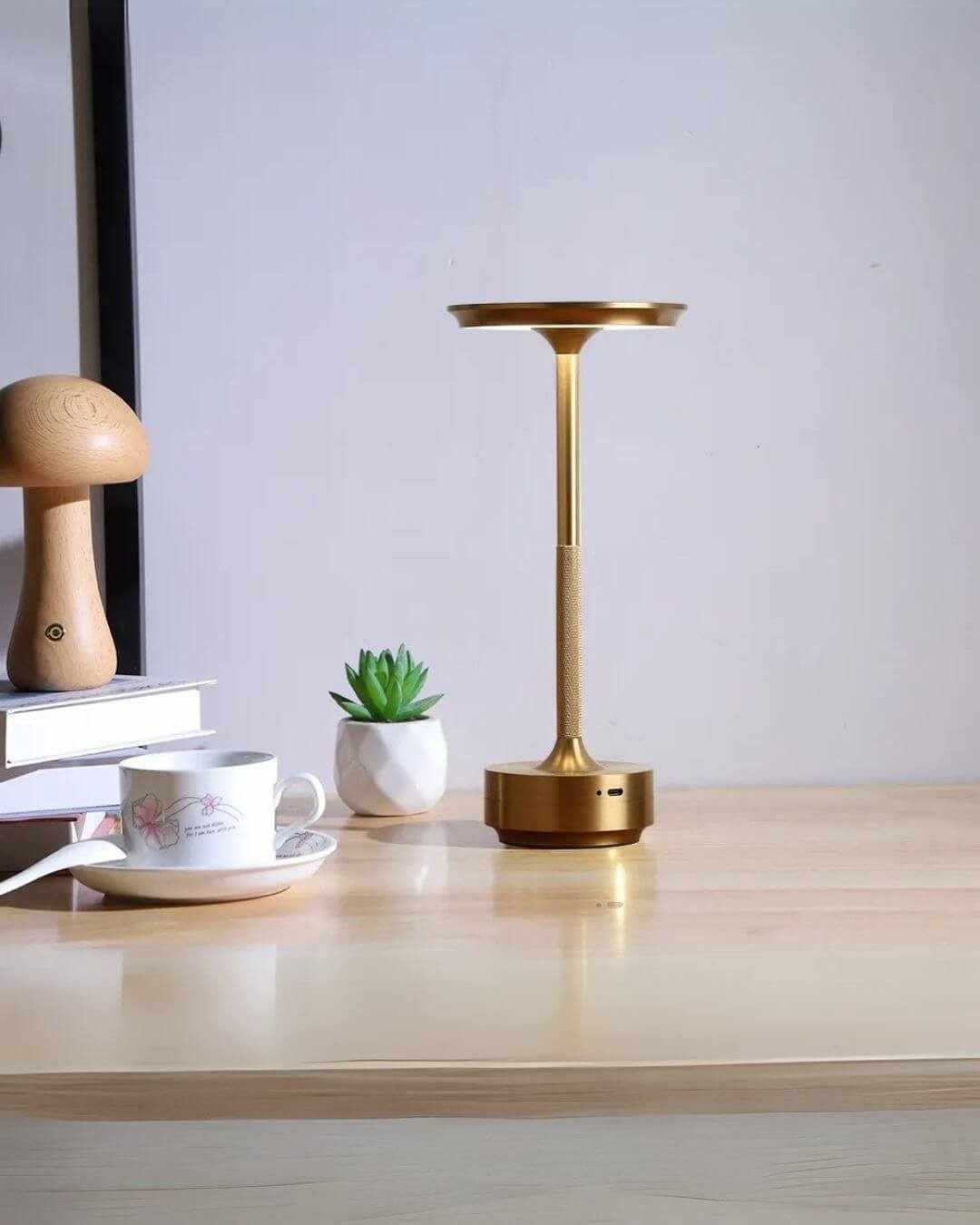 LumiHikari Base Lamp with brushed metal finish on wooden desk next to cup and plant