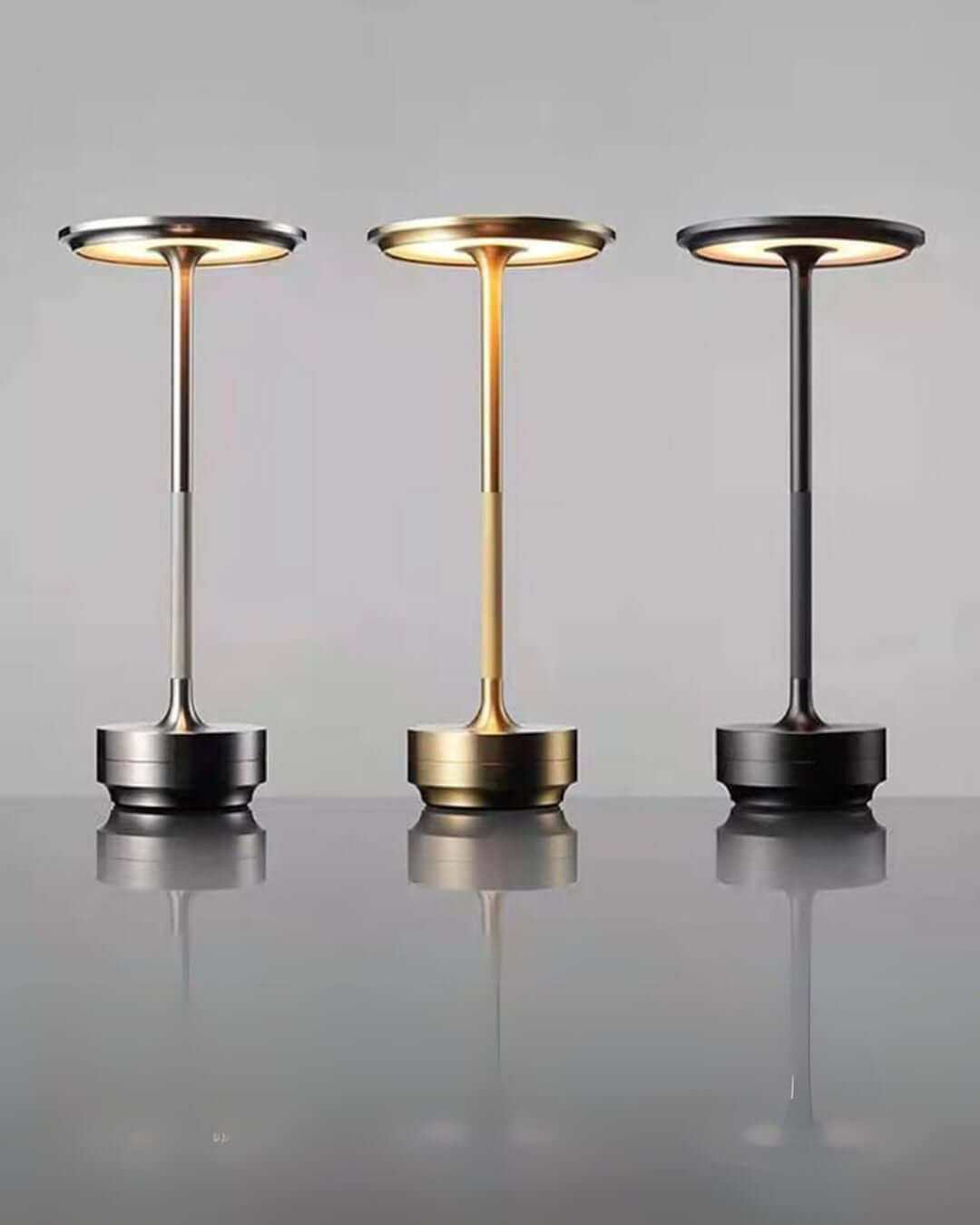 Three LumiHikari Base Lamps in brushed metal finishes showcasing cool, warm, and mixed ambient lighting modes on a reflective surface